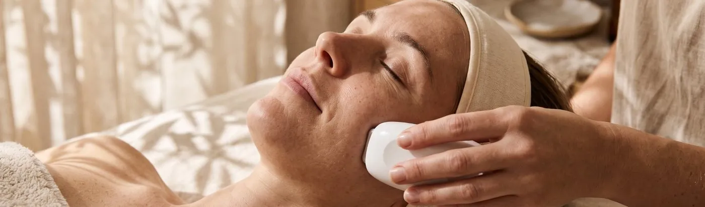 Tratamiento facial con un aparato sobre la mejilla de una clienta relajada